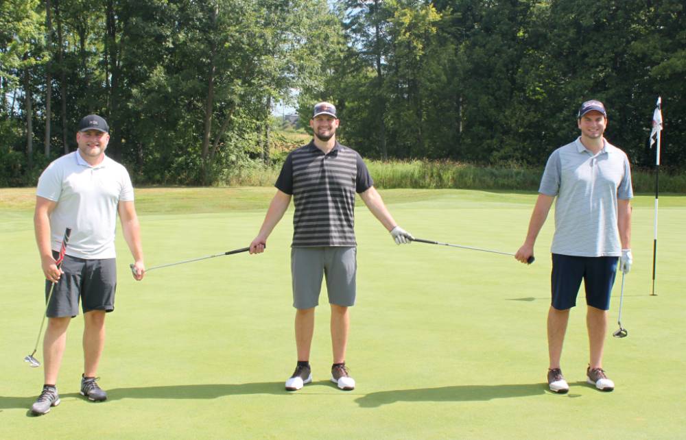 three alumni taking a picture together on the golf course